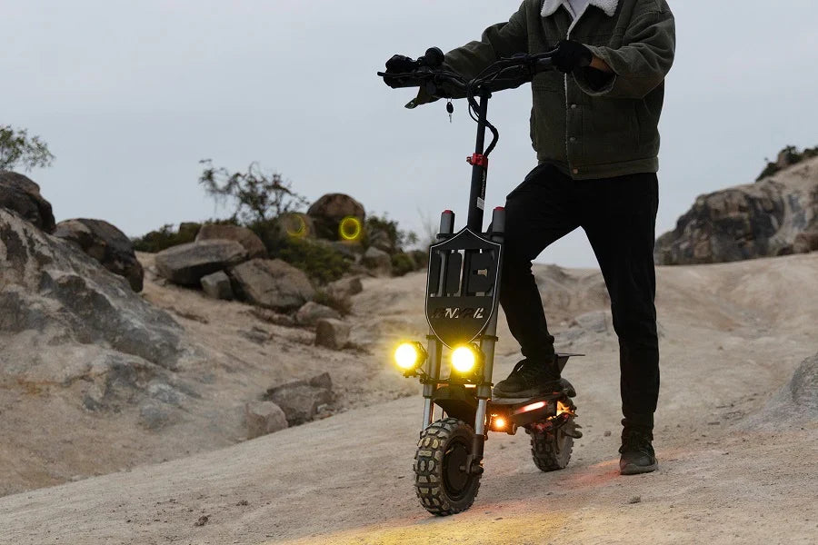 E-Scooter mit eingeschalteten Scheinwerfern in der Dämmerung auf einem felsigen Pfad