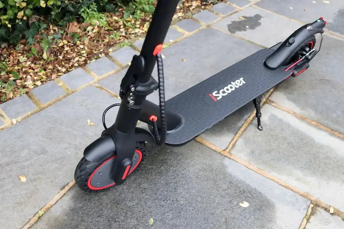 Schwarzer iScooter E-Scooter mit roten Felgenakzenten, auf dem Ständer abgestellt, auf feuchten grauen Steinplatten