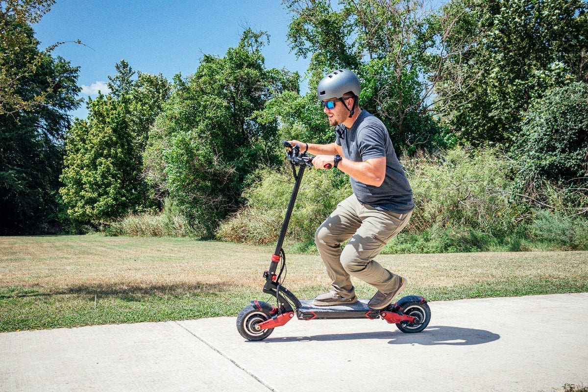 Mann mit Helm und Sonnenbrille auf einem kräftigen E-Scooter mit Federung auf einem Betonweg im Park – Vor- und Nachteile