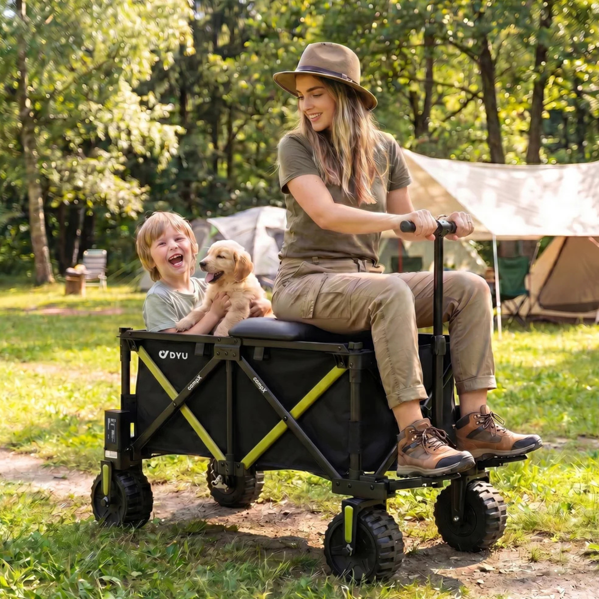 DYU CampX auf dem Rasen neben einem Zelt, eine Frau sitzt auf dem Wagen, ein Kind mit Welpe sitzt darin