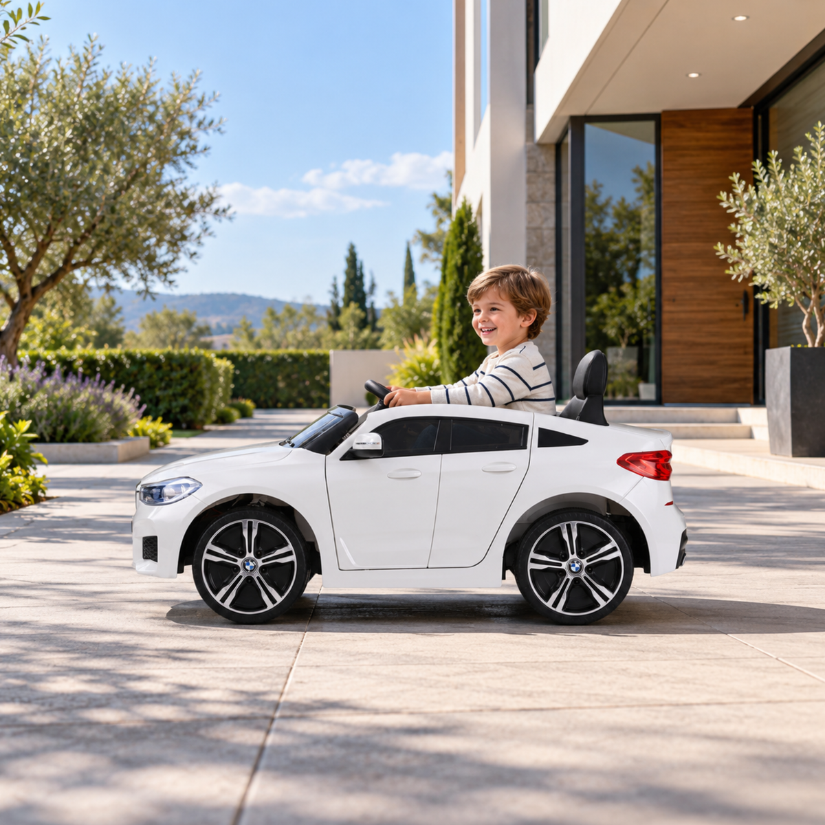 Kind fährt das BMW 6GT Elektroauto für Kinder in Weiß auf einem Fußweg