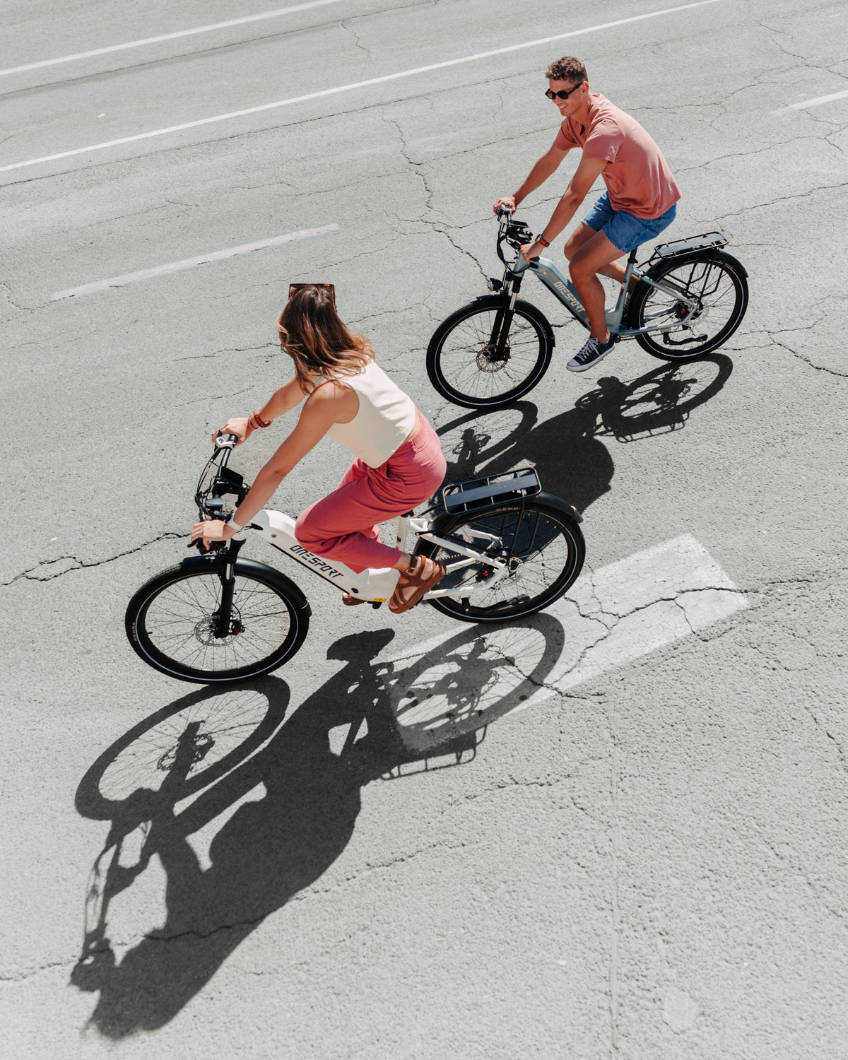 OneSport WT05 von oben gesehen, eine Frau auf einem weißen Fahrrad und ein Mann auf einem grauen Fahrrad fahren auf Asphalt mit Schatten