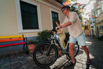 OneSport WT05 in der Seitenansicht, ein Mann hält den Lenker, während eine Frau mit einem Fahrrad dahinter auf einer Straße mit Regenschirmen steht