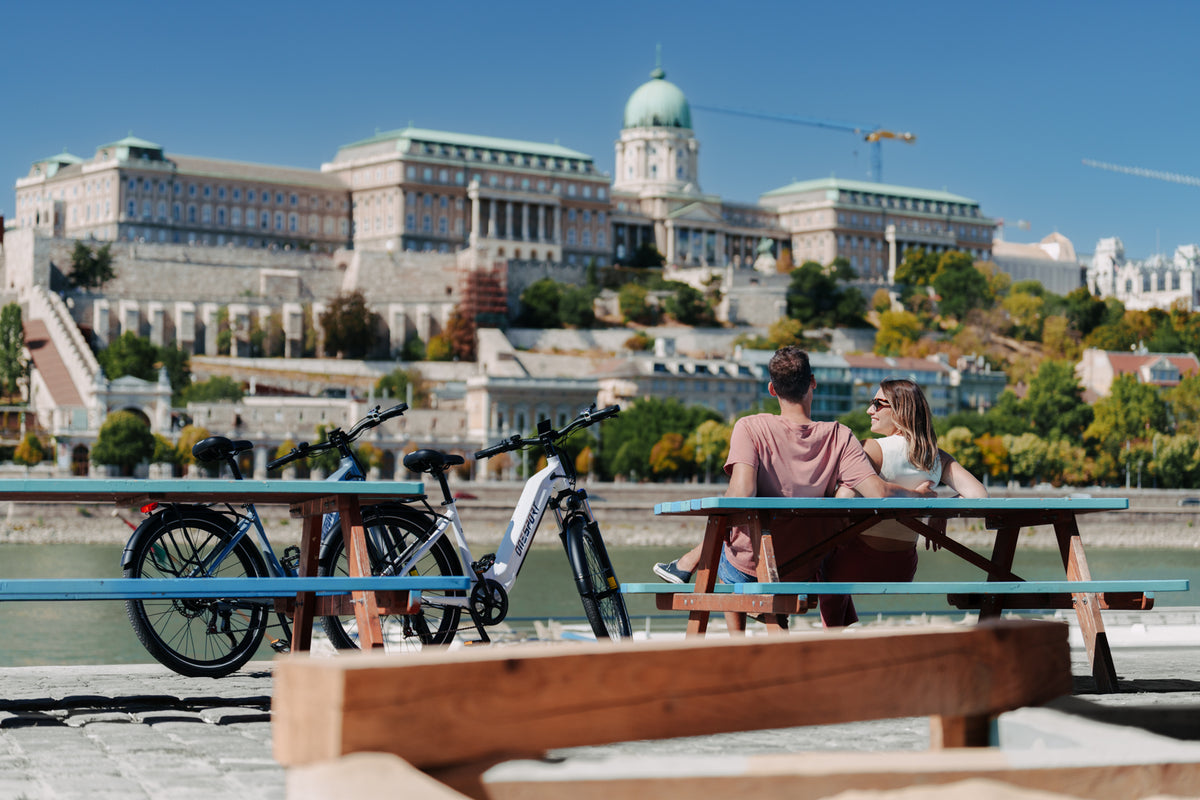 OneSport WT05 geparkt an einem Picknicktisch am Fluss, mit einem Paar und einem Schlossgebäude im Hintergrund