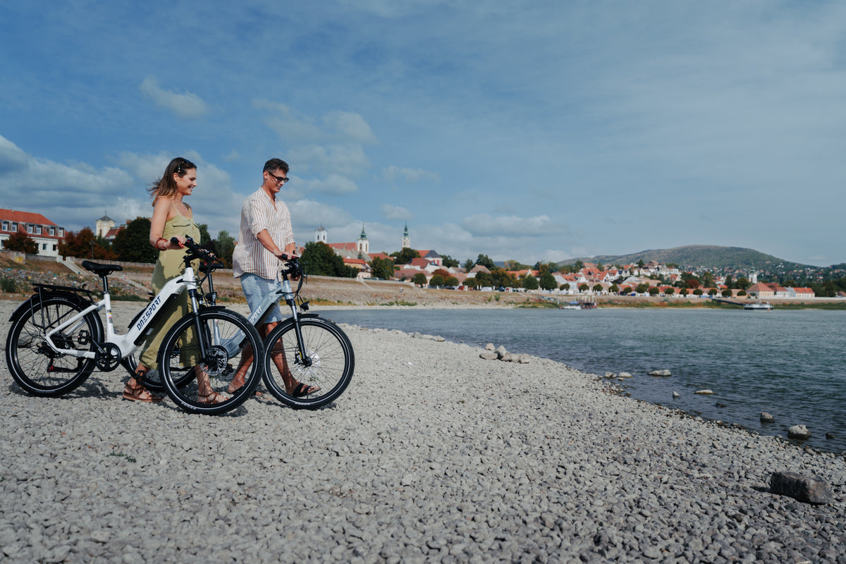 Zwei Personen schieben je ein OneSport WT05 an einem Steinstrand entlang, im Hintergrund Stadt und Hügel