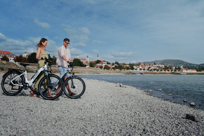 Zwei Personen schieben je ein OneSport WT05 an einem Steinstrand entlang, im Hintergrund Stadt und Hügel