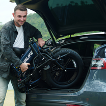 Lächelnder Mann lädt ein zusammengeklapptes URLIFE T5 in die Heckklappe eines Autos