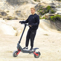 Mann steht neben dem HX X10 E-Scooter auf sandigem Untergrund